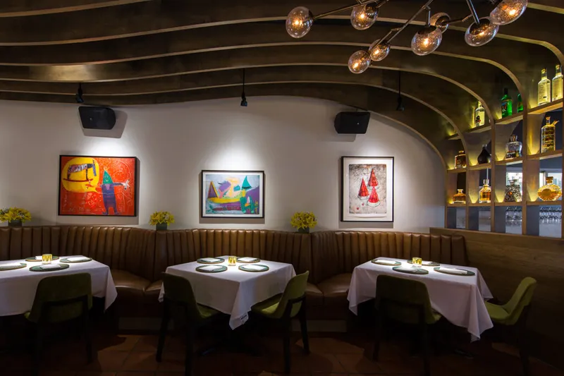 Topolobampo dining room with brown leather banquette, white-clothed tables, green chairs and framed Mexican folk art
