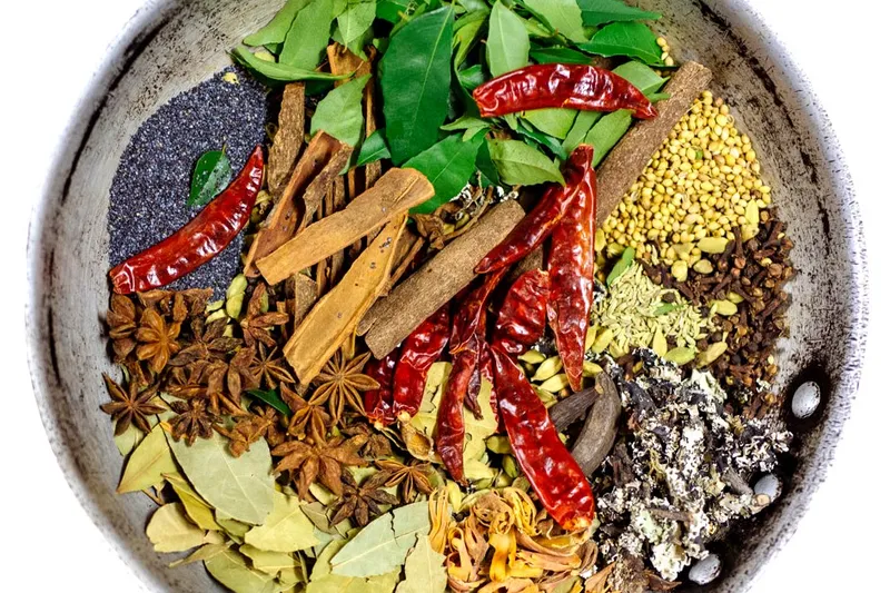 Overhead photo of a metal bowl of whole South Indian spices — curry leaves, dried red chiles, cinnamon, star anise, cardamom, coriander and bay leaves — from Paper Dosa in Santa Fe