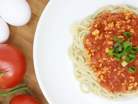 Overhead bowl of Corner 17 hand-pulled noodles topped with house tomato-egg sauce and scallions