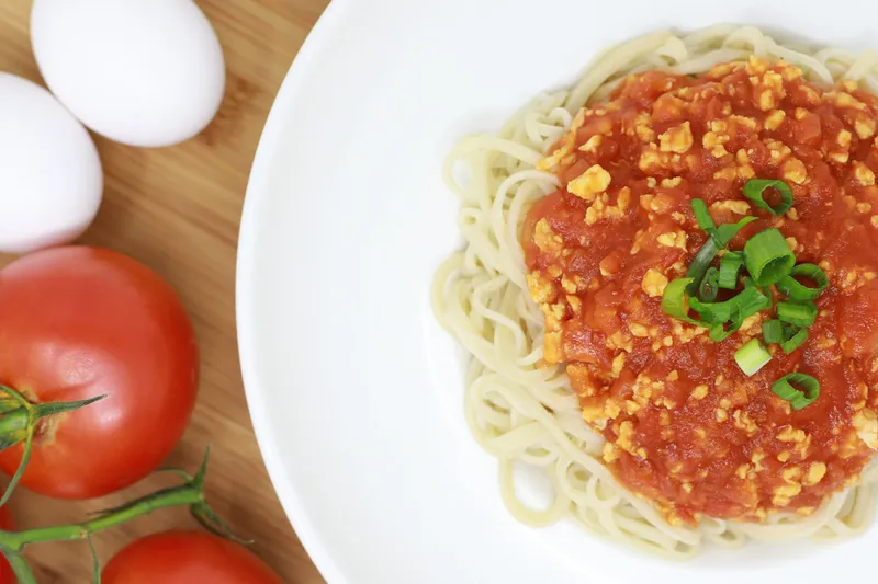 Overhead bowl of Corner 17 hand-pulled noodles topped with house tomato-egg sauce and scallions