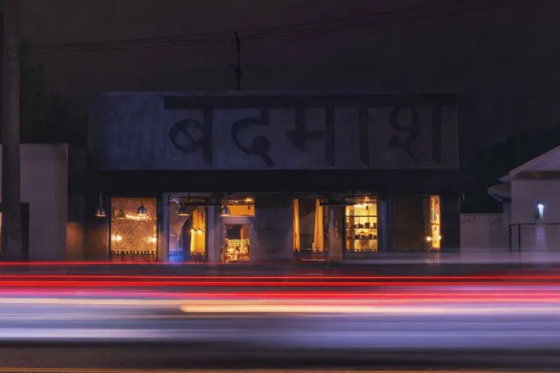 Badmaash DTLA storefront illuminated at night with traffic lights passing in front