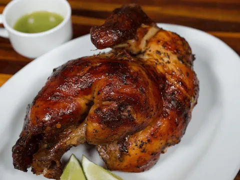 Pollo al carbon (rotisserie chicken) served with green sauce and lime wedges at El Malecon