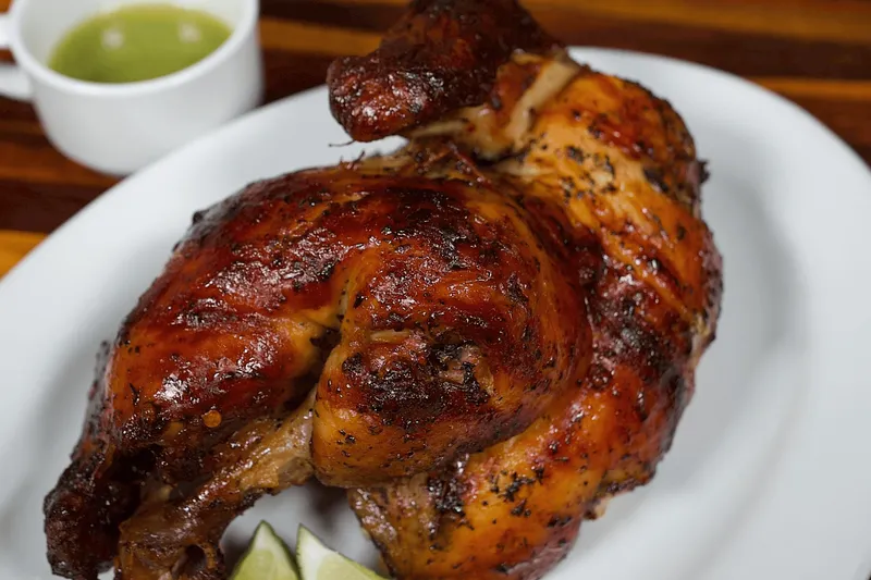 Pollo al carbon (rotisserie chicken) served with green sauce and lime wedges at El Malecon