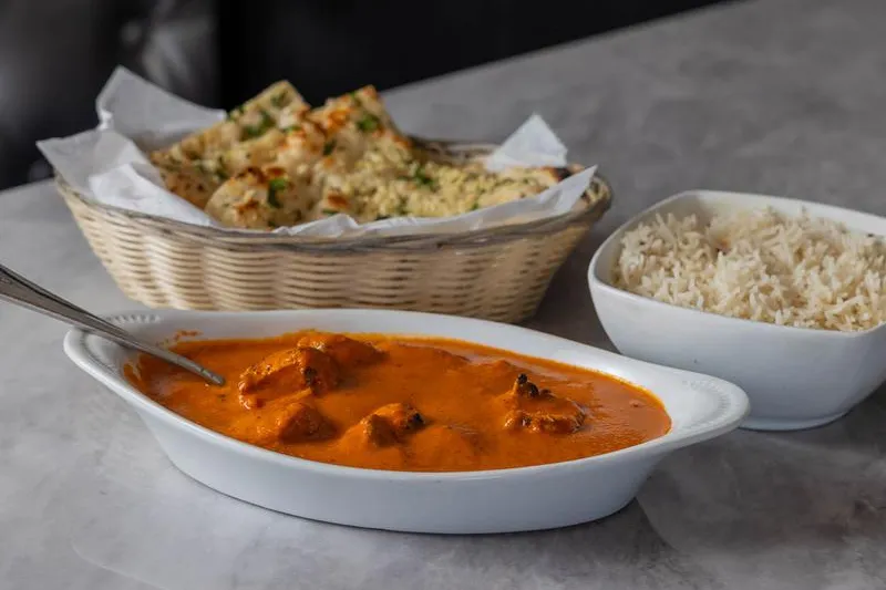 Asiana Indian Cuisine chicken tikka masala in a white dish served with a basket of garlic naan and a bowl of basmati rice
