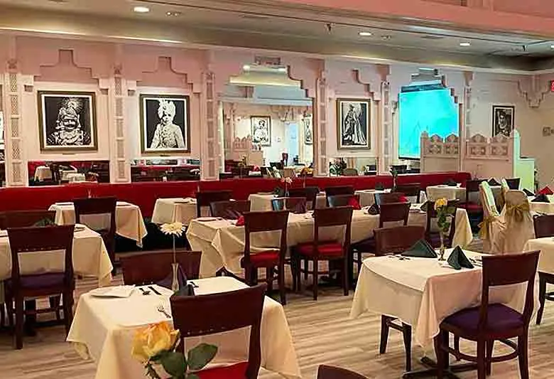 The renovated dining room at Royal India in Raleigh, with white-clothed tables, dark wood chairs, arched pink pillars and framed Rajasthani portraits on the walls