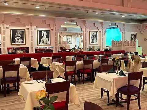 The renovated dining room at Royal India in Raleigh, with white-clothed tables, dark wood chairs, arched pink pillars and framed Rajasthani portraits on the walls
