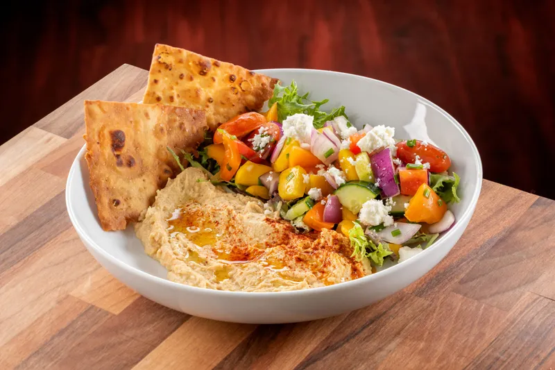 Bowl of hummus drizzled with olive oil and paprika, served with toasted pita wedges and a chopped vegetable salad, at Union Grill in Pittsburgh