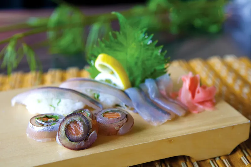 Sashimi plated on a wooden board with shiso, pickled ginger and lemon at Sushi Kashiba, Seattle