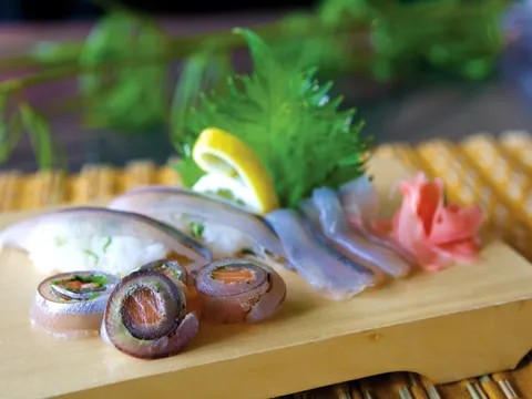 Sashimi plated on a wooden board with shiso, pickled ginger and lemon at Sushi Kashiba, Seattle