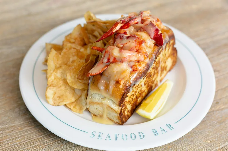 Warm New England lobster roll on a buttered split-top bun with potato chips and lemon on a Saltie Girl Seafood Bar plate