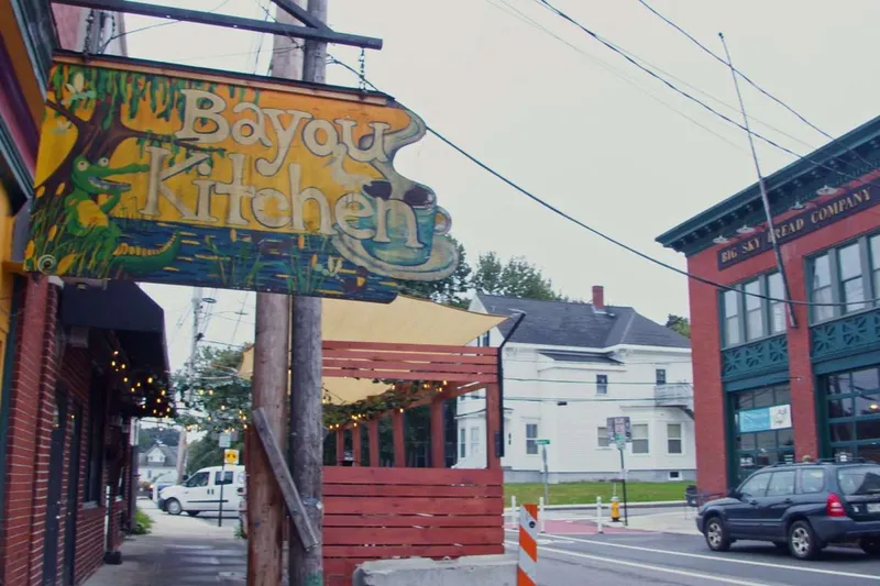 Carved wooden sign for The Bayou Kitchen hanging over a Portland street corner