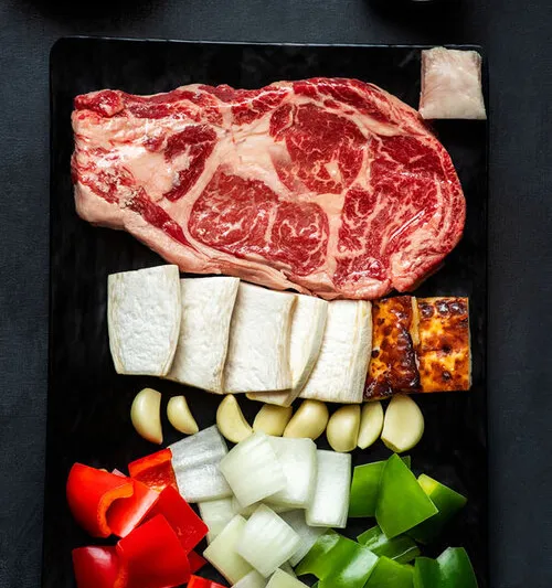 Cast-iron prime ribeye platter with garlic, onion and peppers ready for the grill at Kang Ho Dong Baekjeong