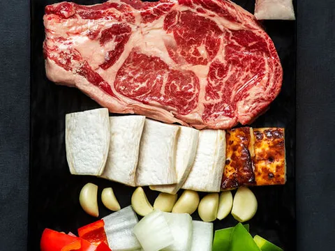 Cast-iron prime ribeye platter with garlic, onion and peppers ready for the grill at Kang Ho Dong Baekjeong