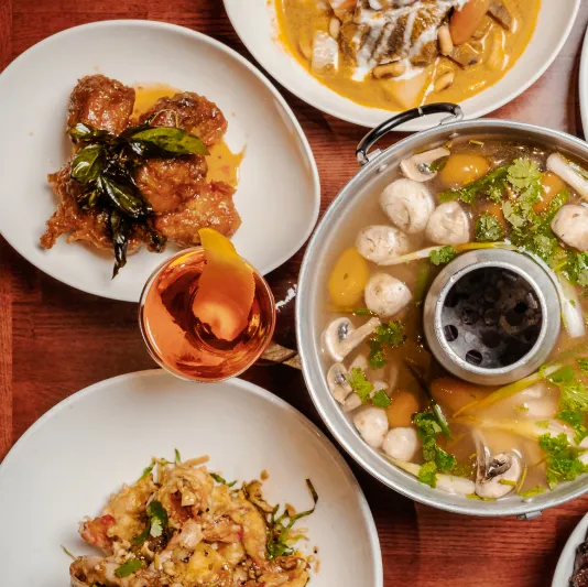 Spread of Lotus of Siam dishes, including a curry, a tom yum hot pot, and crispy seafood, on a wooden table