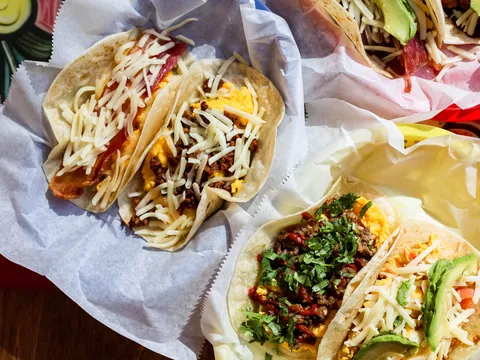 A paper-lined basket of Tacodeli breakfast tacos on corn and flour tortillas — bacon and egg, chorizo and picadillo with shredded cheese, cilantro and avocado