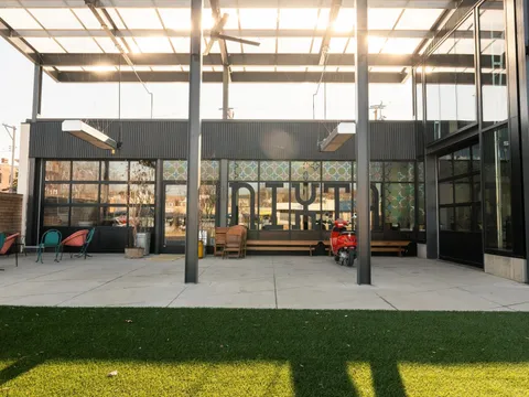 Exterior patio of Nixta in St. Louis at dusk, with the NIXTA name across the tiled storefront windows, wooden benches, and a red scooter parked under a steel canopy