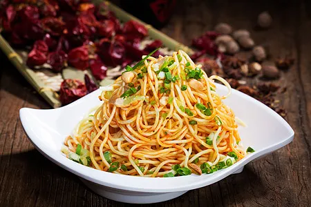 A bowl of Sichuan Tasty's chili-oil noodles topped with scallions, set beside dried red chilies