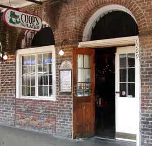The brick French Quarter storefront of Coop's Place on Decatur Street with its alligator sign and open wooden door