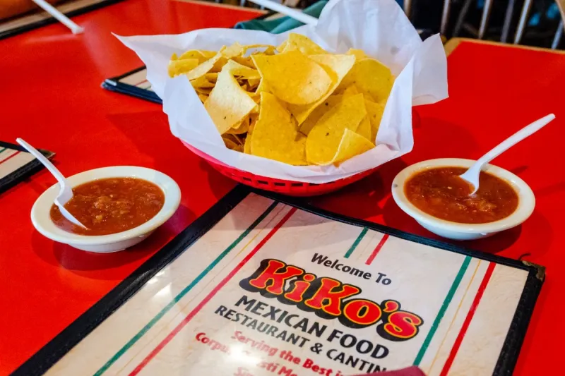 Basket of tortilla chips with two bowls of red salsa beside a Kiko's Mexican Food Restaurant & Cantina table menu