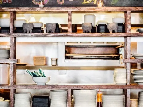 Rustic wooden shelving stacked with plates below a hand-chalked "Sangria del Día" board inside Bodega Taco Bar in Fairfield, Connecticut
