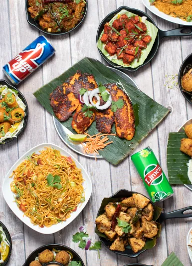 Overhead spread of Godavari dishes including biryani, tawa fish fry, gobi and paneer starters, chicken and idli on a wooden table