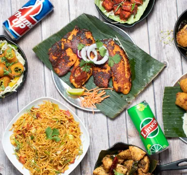 Overhead spread of Godavari dishes including biryani, tawa fish fry, gobi and paneer starters, chicken and idli on a wooden table