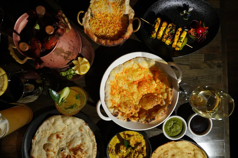 An overhead spread of Indian dishes at Roti Cuisine of India including biryani, tandoori chicken, paneer skewers, curries and naan