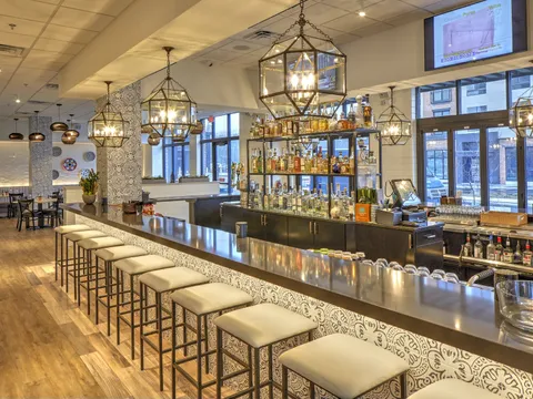 Interior bar at El Camino Mexican Kitchen in Wilmington, Delaware, with white barstools, patterned tilework and a lit back wall of tequila bottles