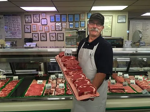 Butcher holding a tray of fresh-cut steaks at the Corralitos Market meat counter