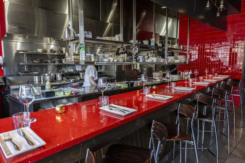 Open-kitchen counter with a red quartz chef's bar, place settings and stools at Nick's on Broadway in Providence