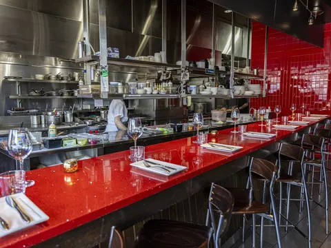 Open-kitchen counter with a red quartz chef's bar, place settings and stools at Nick's on Broadway in Providence