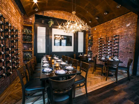 Exposed-brick private dining room with a long set table and wine racks at Paisley in Tribeca
