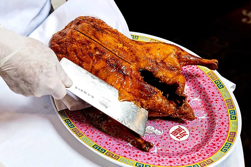A whole roast Peking duck being carved tableside on a decorated porcelain platter at Peking Gourmet Inn