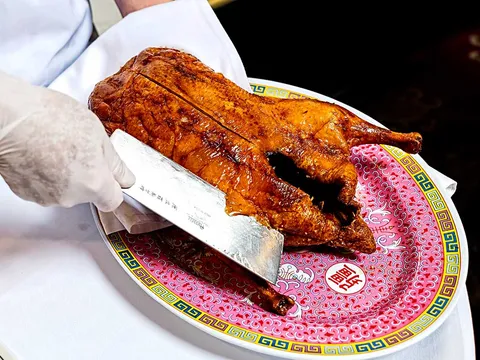A whole roast Peking duck being carved tableside on a decorated porcelain platter at Peking Gourmet Inn