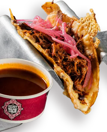 Quesa Birria taco with pulled pork and pickled onion in a griddled tortilla beside a cup of birria consome at Velvet Taco
