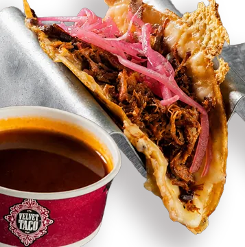 Quesa Birria taco with pulled pork and pickled onion in a griddled tortilla beside a cup of birria consome at Velvet Taco