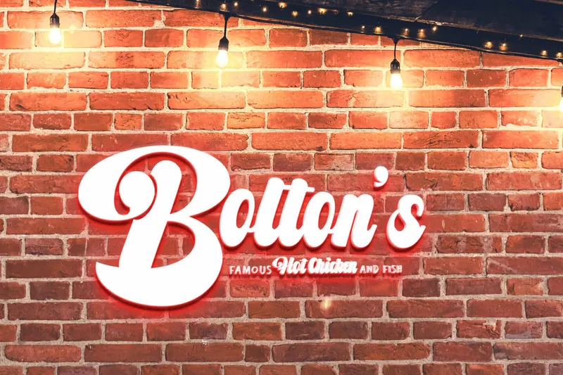 Illuminated Bolton's Famous Hot Chicken and Fish sign mounted on the exposed brick wall inside the restaurant