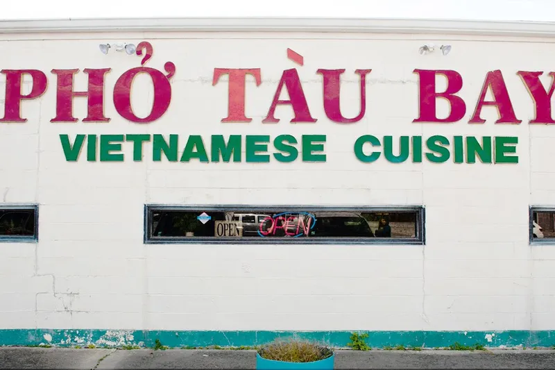 Whitewashed storefront of Pho Tau Bay Vietnamese Cuisine on Tulane Avenue in New Orleans, with a lit OPEN sign in the window
