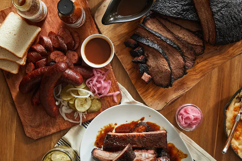 Overhead spread of sliced brisket, house sausage, pork ribs, pickles and white bread on wood boards at Lewis Barbecue in Charleston