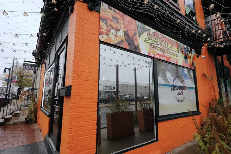 Orange brick corner exterior of Merengue House Restaurant & Bar strung with patio lights