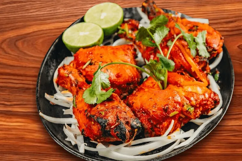 Plate of tandoori chicken garnished with cilantro and lime over sliced onions at Bombay House in Tempe.