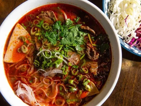 Bowl of bun bo Hue spicy beef noodle soup with herbs at Madame Vo