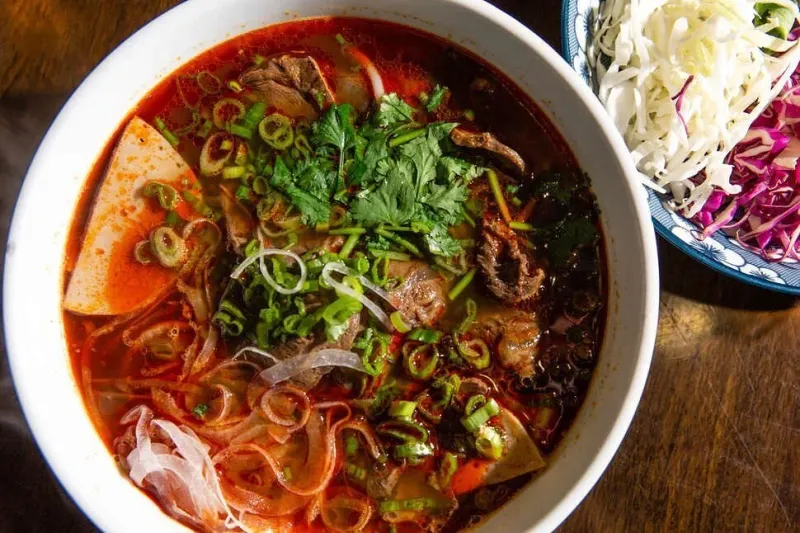 Bowl of bun bo Hue spicy beef noodle soup with herbs at Madame Vo