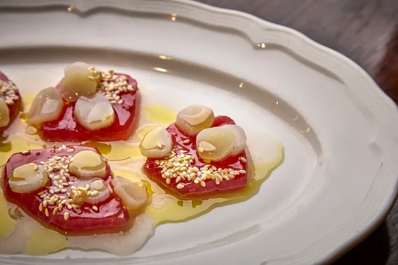 Bluefin tuna crudo with sesame seeds, sliced garlic and olive oil on a white fluted platter at Alla Vita in Nashville