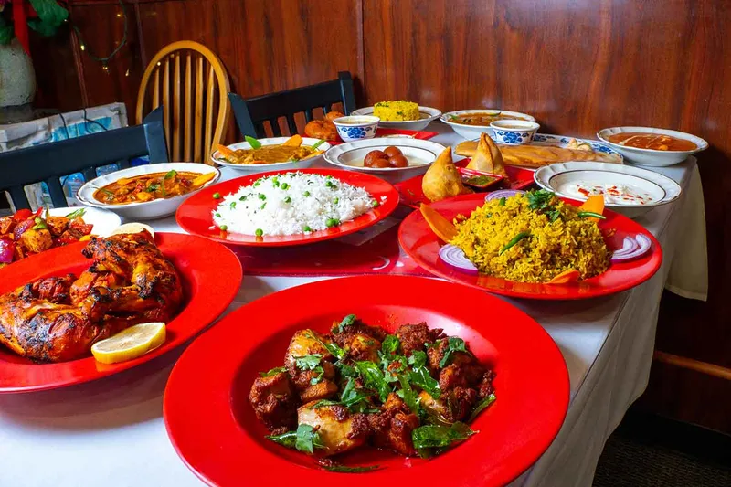 Table laid with curries, rice and appetizers on red plates at Chili's South Indian Cuisine