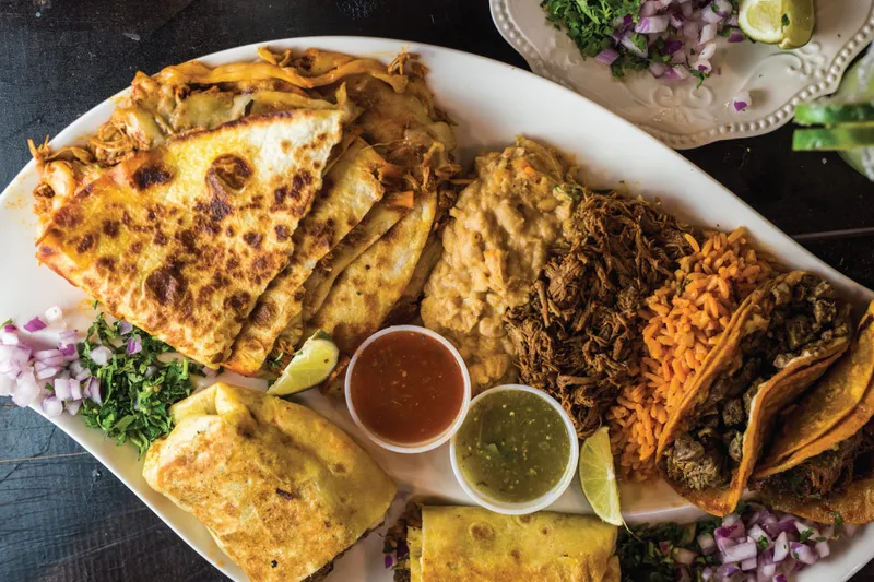 Quesabirria tacos and consomme on a platter at Chucho's Red Tacos