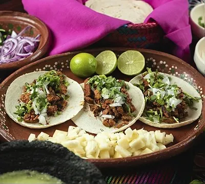 Three tacos topped with chopped meat, onion, and cilantro on a brown ceramic platter at Jaime's Mexican Restaurant