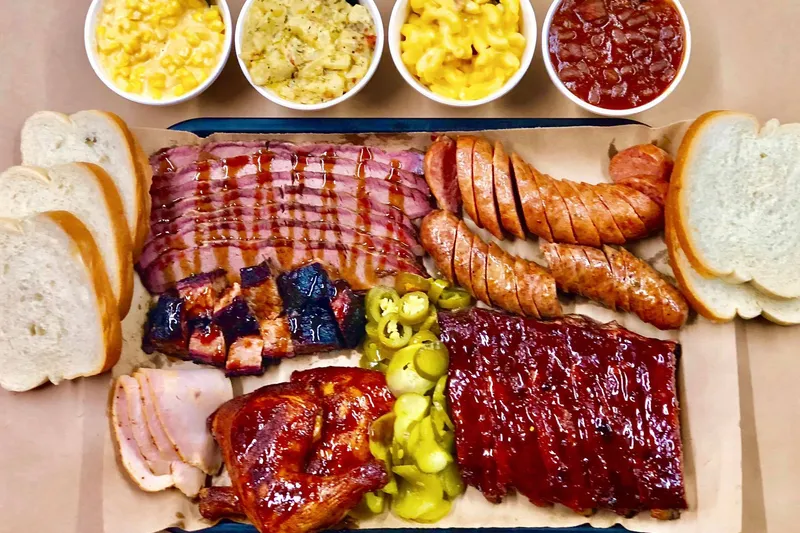 Slap's BBQ sampler platter with sliced brisket, burnt ends, sausage, ribs, smoked chicken, ham, pickles and sides