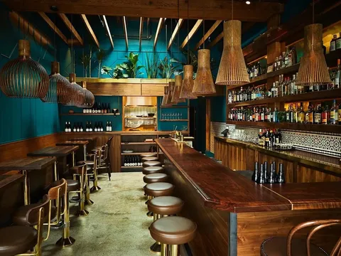 Bar at Rupee Bar, with teal panelling, brass pendant lights and a row of stools