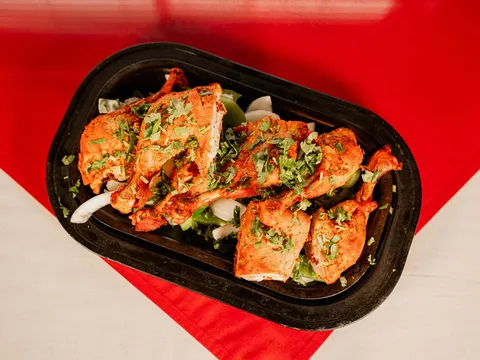 Tandoori chicken pieces garnished with cilantro served on a black platter at Amul India Restaurant